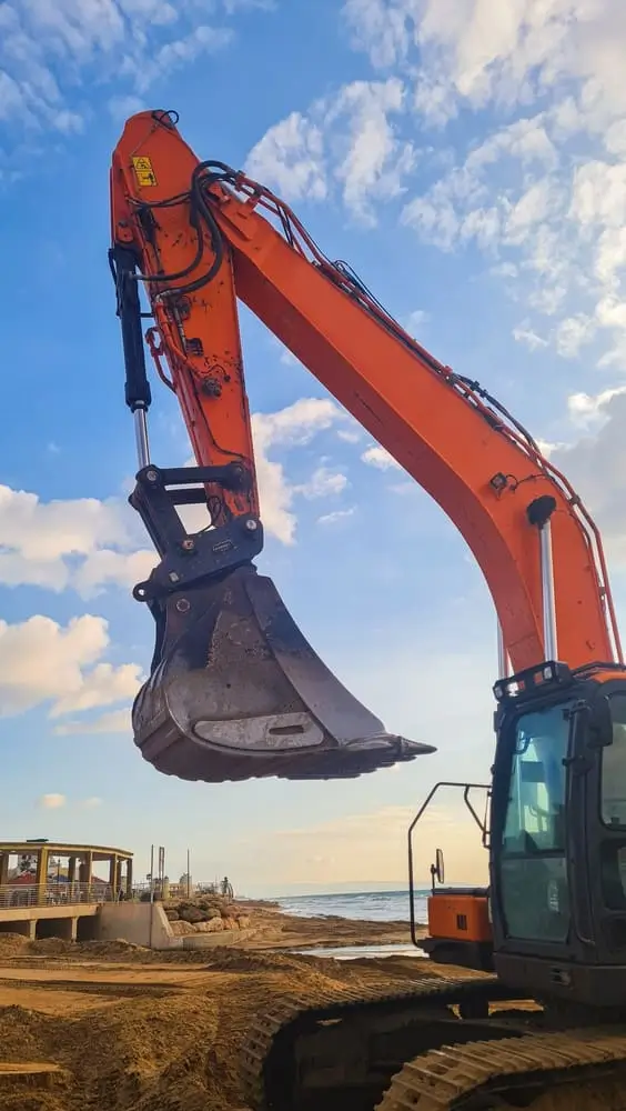Stabilisateurs d'une lourde pelle hydraulique positionnés sur un rivage rocheux pour des travaux de protection côtière.